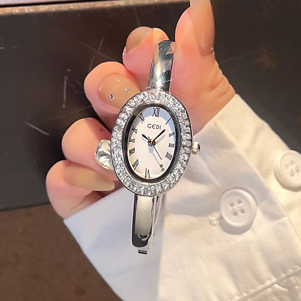 Silver wristwatch with gemstones held by a person wearing a white shirt.
