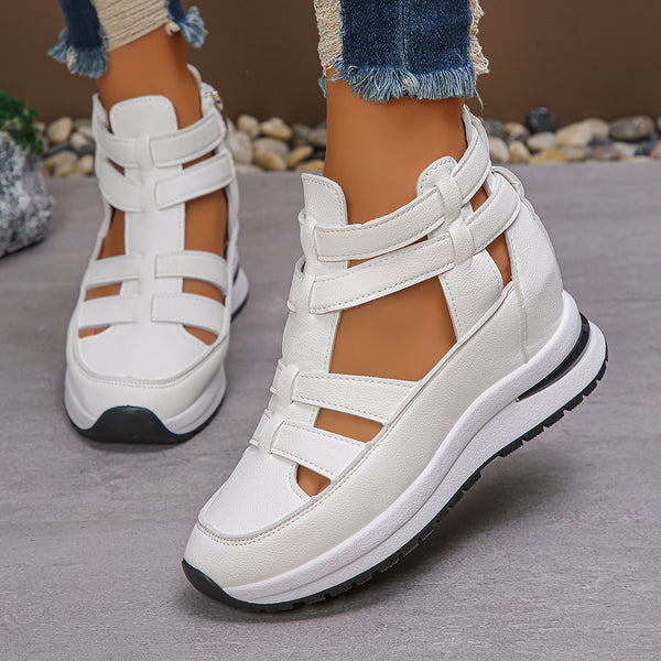 White strappy sandals with black soles worn by a person on a gray surface.