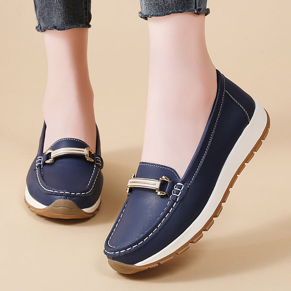 Navy blue loafers with gold accents worn by a person on a beige background