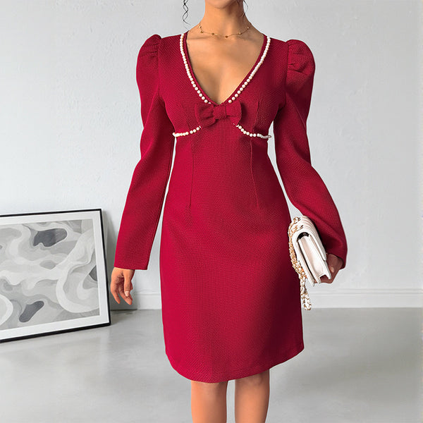 Red dress with pearl details worn by a person, holding a white handbag against a plain background.