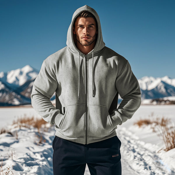 Man wearing a gray hoodie standing in a snowy landscape with mountains in the background