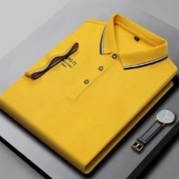 Yellow polo shirt with a watch and pen on a gray surface