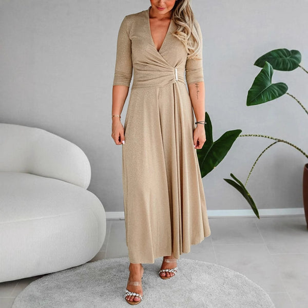 Woman wearing a beige wrap dress in a modern room with a plant and gray sofa.