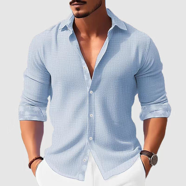 Man wearing a light blue button-up shirt with rolled-up sleeves on a plain background