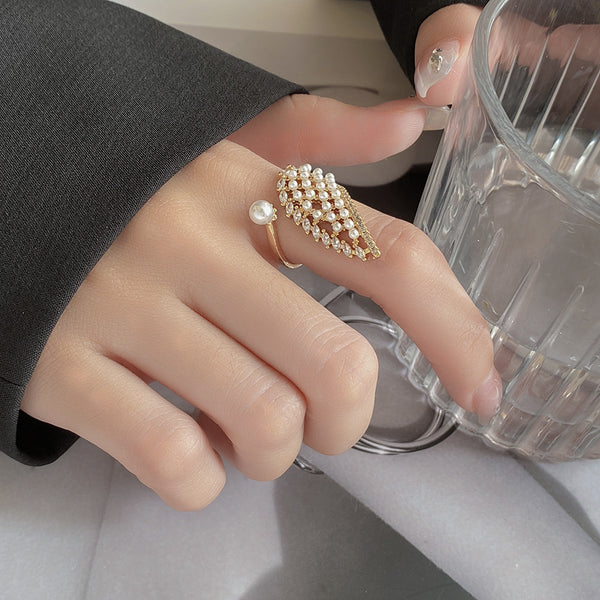 Hand wearing a pearl ring holding a clear glass cup.