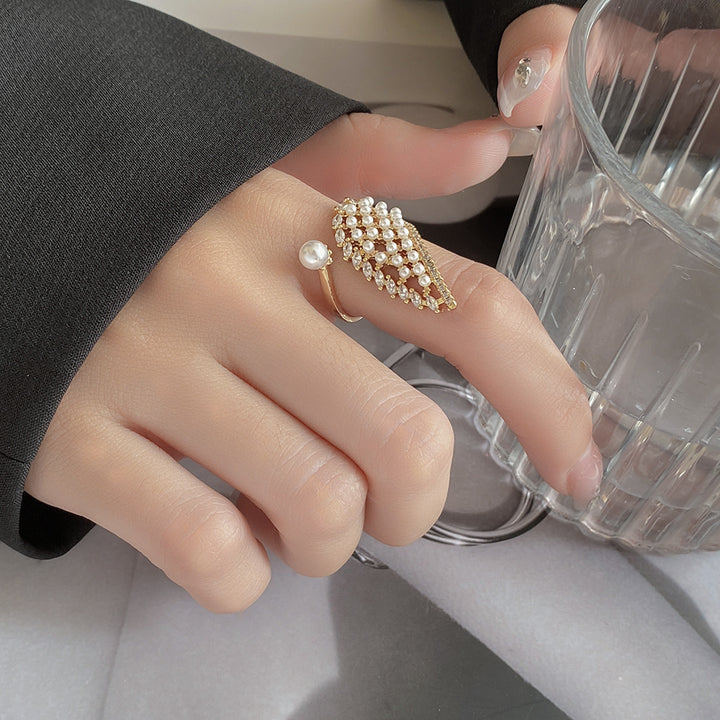 Hand wearing a pearl ring holding a clear glass cup.