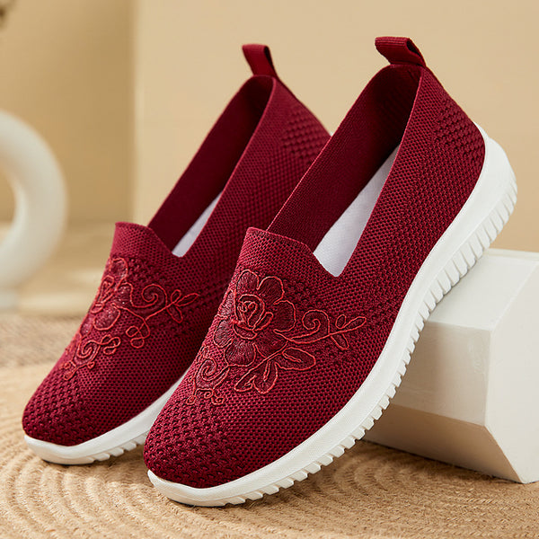Red slip-on shoes with floral embroidery on a beige background
