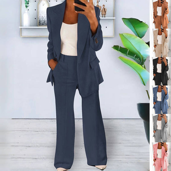 Woman wearing a navy blue Women’s Lapel Blazer & Slim-Fit Trousers Set with a white top, standing in a room with a plant and shelves